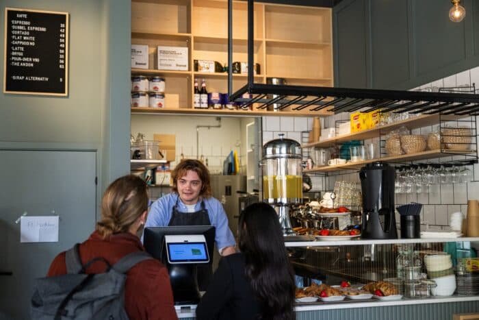 Barista behind a modern cafe counter taking an order from two customers.