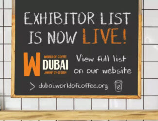 A chalkboard sign announces that the exhibitor list for World of Coffee Dubai 2024 is now live, with event details and website link.