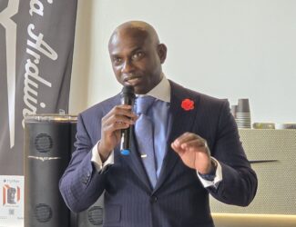 Mr. Garfield Kerr speaking at the UAE Coffee Innovation Summit in Dubai, holding a microphone while addressing the audience.