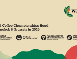 Promotional banner for the 2026 World Coffee Championships. The text reads “World Coffee Championships Head to Bangkok & Brussels in 2026,” with logos for four competitions: World Cup Tasters Championship, World Brewers Cup, World Coffee in Good Spirits Championship, and World Coffee Roasting Championship. The WCC logo appears at the top right, with colorful abstract shapes along the bottom.