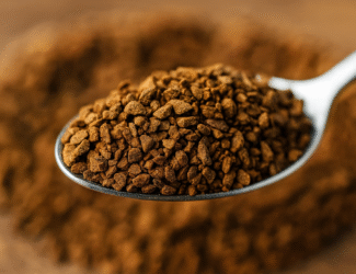Close-up view of instant coffee granules in a glass jar, showing their coarse texture and rich brown color.