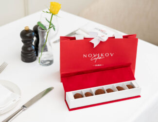 Elegant red Novikov Café gift box with handcrafted chocolates on a white table, presented for Emirati Women’s Day 2025 celebration in Dubai Mall.
