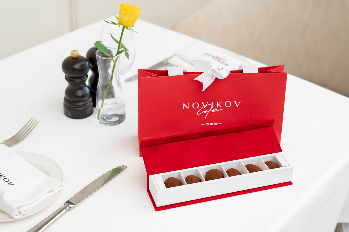 Elegant red Novikov Café gift box with handcrafted chocolates on a white table, presented for Emirati Women’s Day 2025 celebration in Dubai Mall.