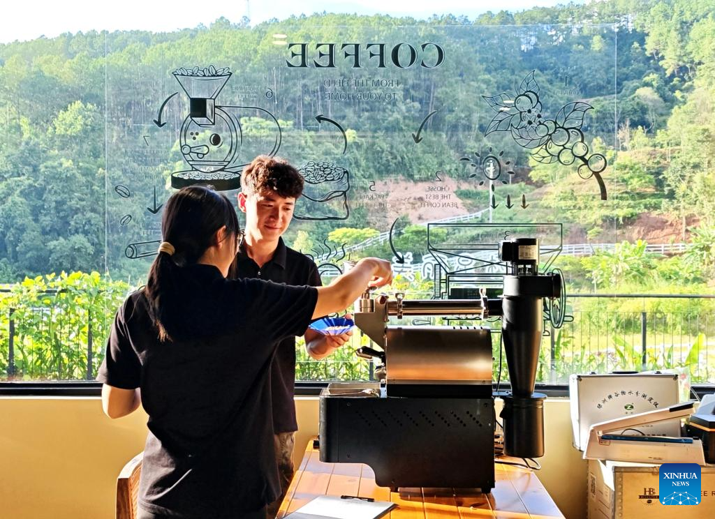 Two staff members roast coffee beans at a café in Nandaohe Village, Pu’er, Yunnan Province, with green hills visible through the window.