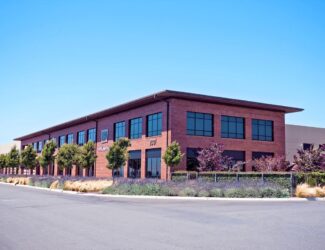 Exterior view of Peet’s Coffee headquarters with modern brick architecture, green landscaping, and clear blue sky.