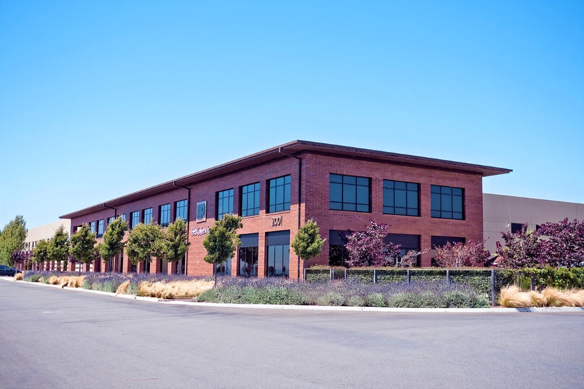Exterior view of Peet’s Coffee headquarters with modern brick architecture, green landscaping, and clear blue sky.