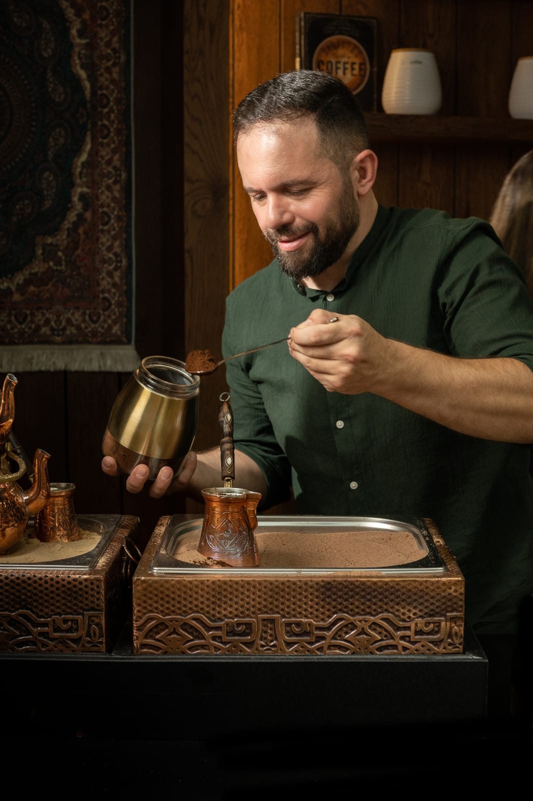 Mahmoud Izachman prepares traditional coffee with care, using a copper cezve over hot sand in a warm, wood-decorated setting — a moment that reflects the artistry and heritage of Palestinian coffee culture.
