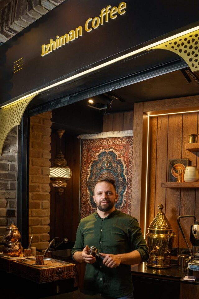Mahmoud Izachman stands at the entrance of Izhiman Coffee in Jerusalem, surrounded by traditional decor and copper coffee equipment, representing a blend of heritage and modern specialty coffee culture.