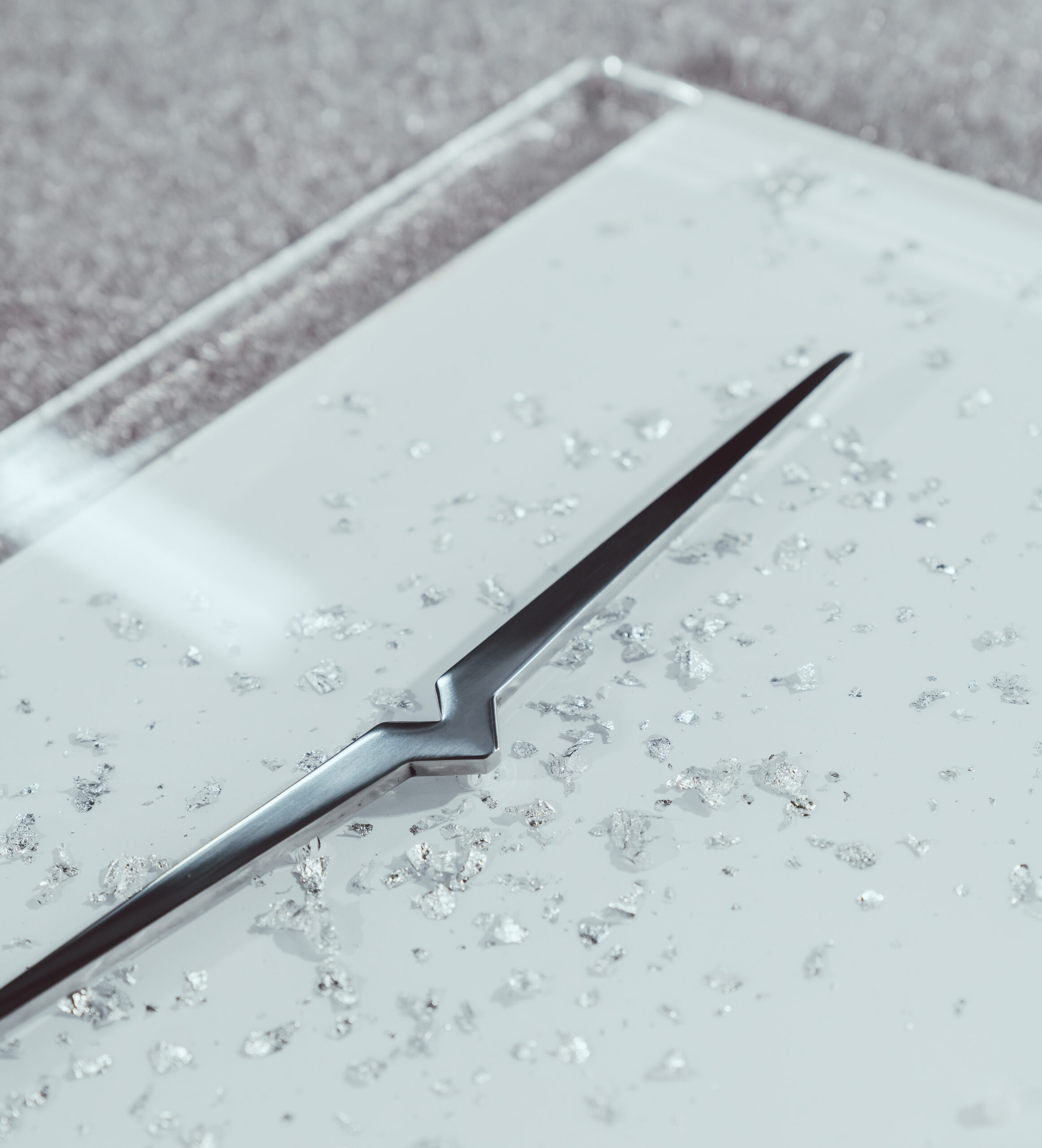 Close-up of a sleek metallic Victoria Arduino design element embedded in a white surface with silver crystal-like fragments, symbolizing luxury craftsmanship and precision.