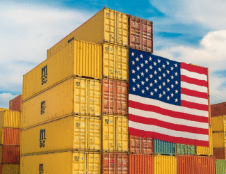 Stacked shipping containers with a large U.S. flag draped across them, symbolizing American trade and import tariffs.